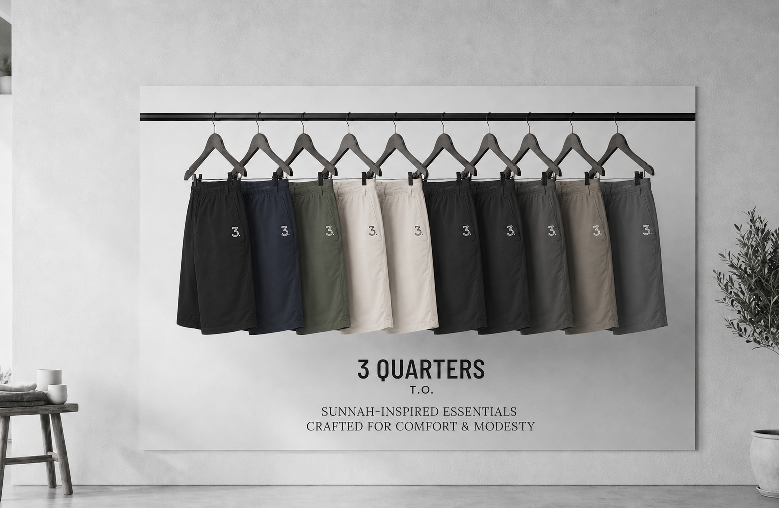 A wall-mounted display showing a row of men's shorts hanging on black hangers against a light gray wall. The shorts come in multiple colors including black, navy, olive, cream, charcoal, and taupe.